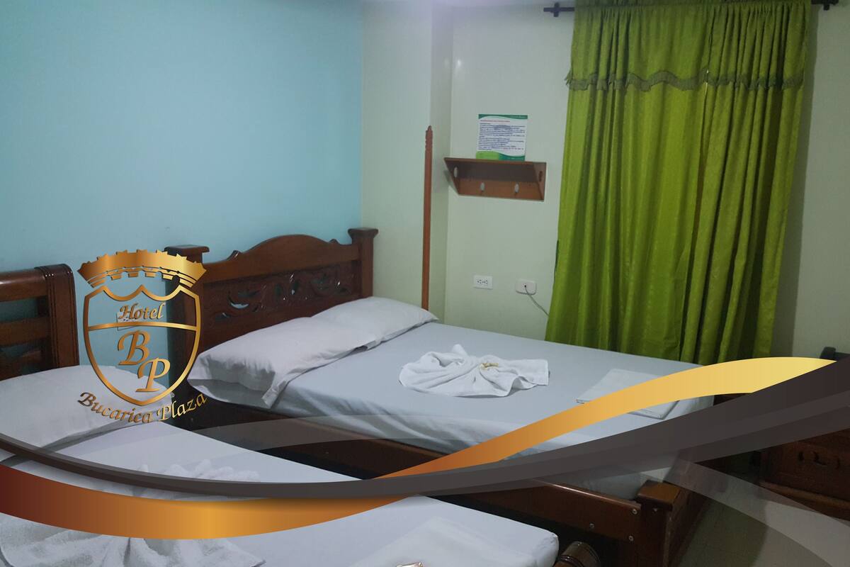 A hotel room with two beds, a wooden headboard, a green curtain, and a wall-mounted shelf.