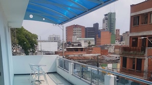 Eine Dachterrasse mit blauem Sonnensegel, Glasgeländer und Blick auf die Stadt.