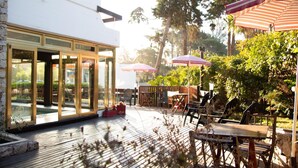 Un patio con mobiliario exterior, sombrillas y una entrada con cerramiento de vidrio.