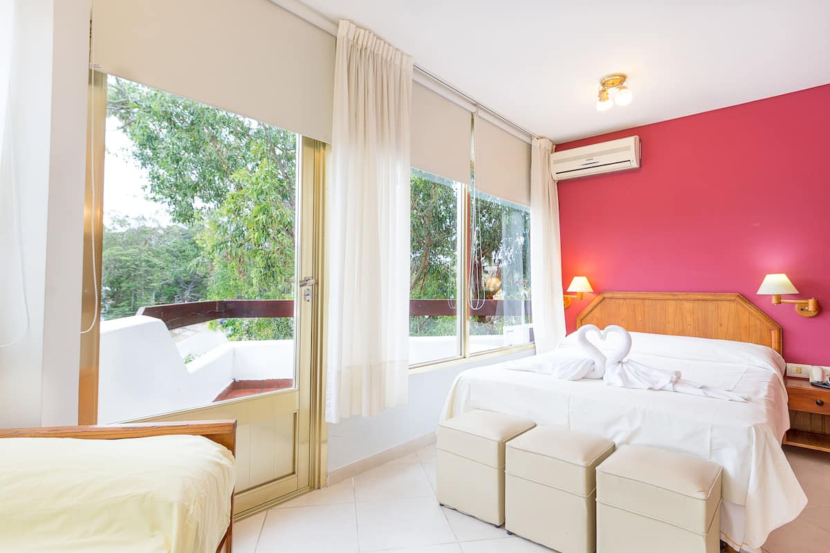 A hotel room with a bed, a seating area, and large windows offering a view of greenery.