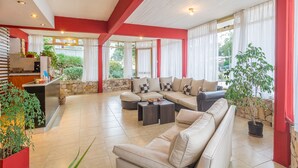 Amplia sala de estar con un sofá grande, una mesa de centro y una zona de cocina con pared de piedra y plantas en macetas.