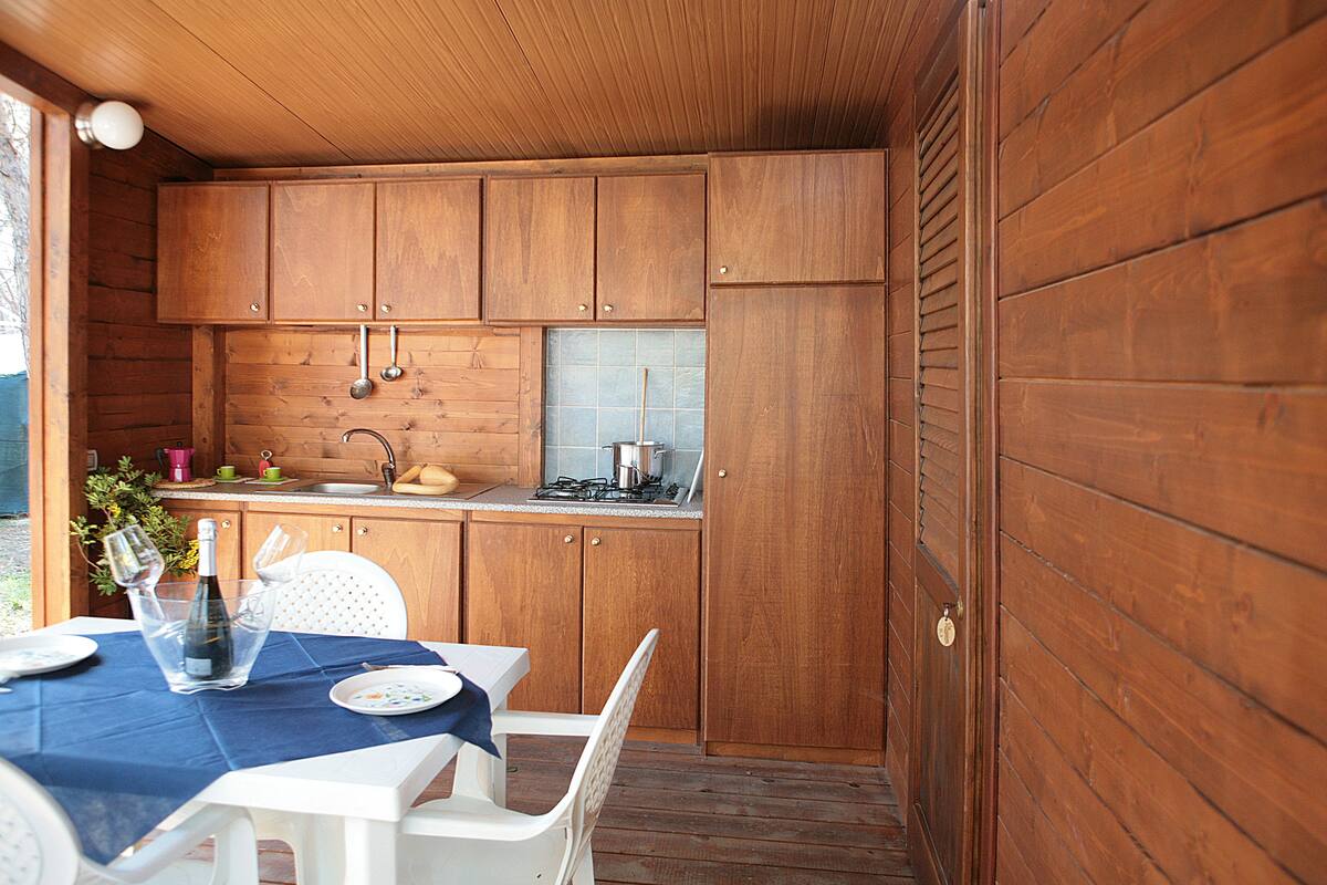A wooden kitchen with a sink, stove, and cabinets. There is a table with a blue tablecloth and chairs.