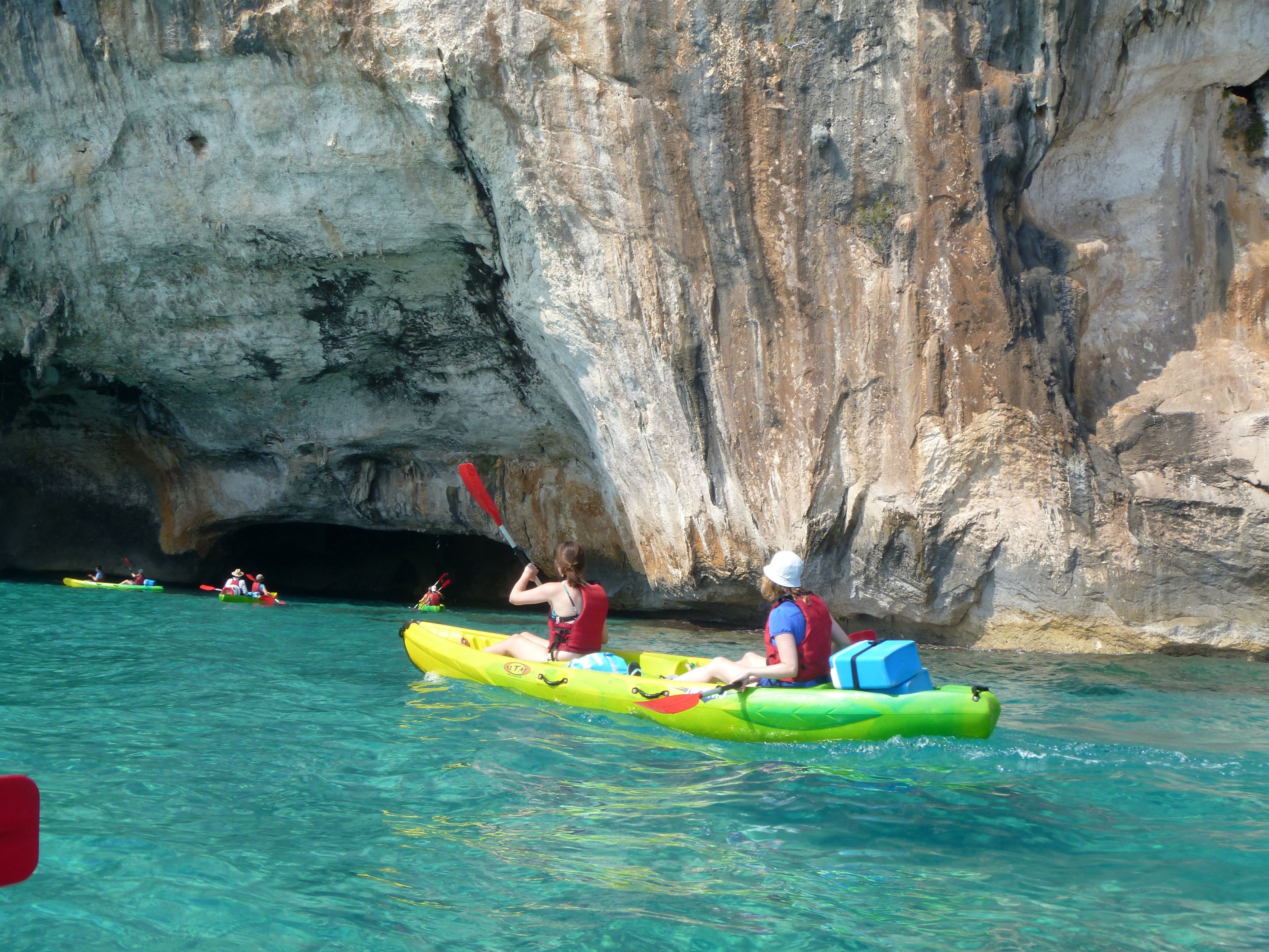 A group of people kayaking in clear water near a rocky cave.