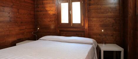 A wooden cabin room with a bed, a nightstand, and a window.