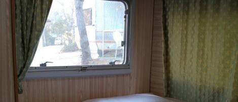 A single bed with a floral bedspread in a cabin with wooden walls and a window with curtains.