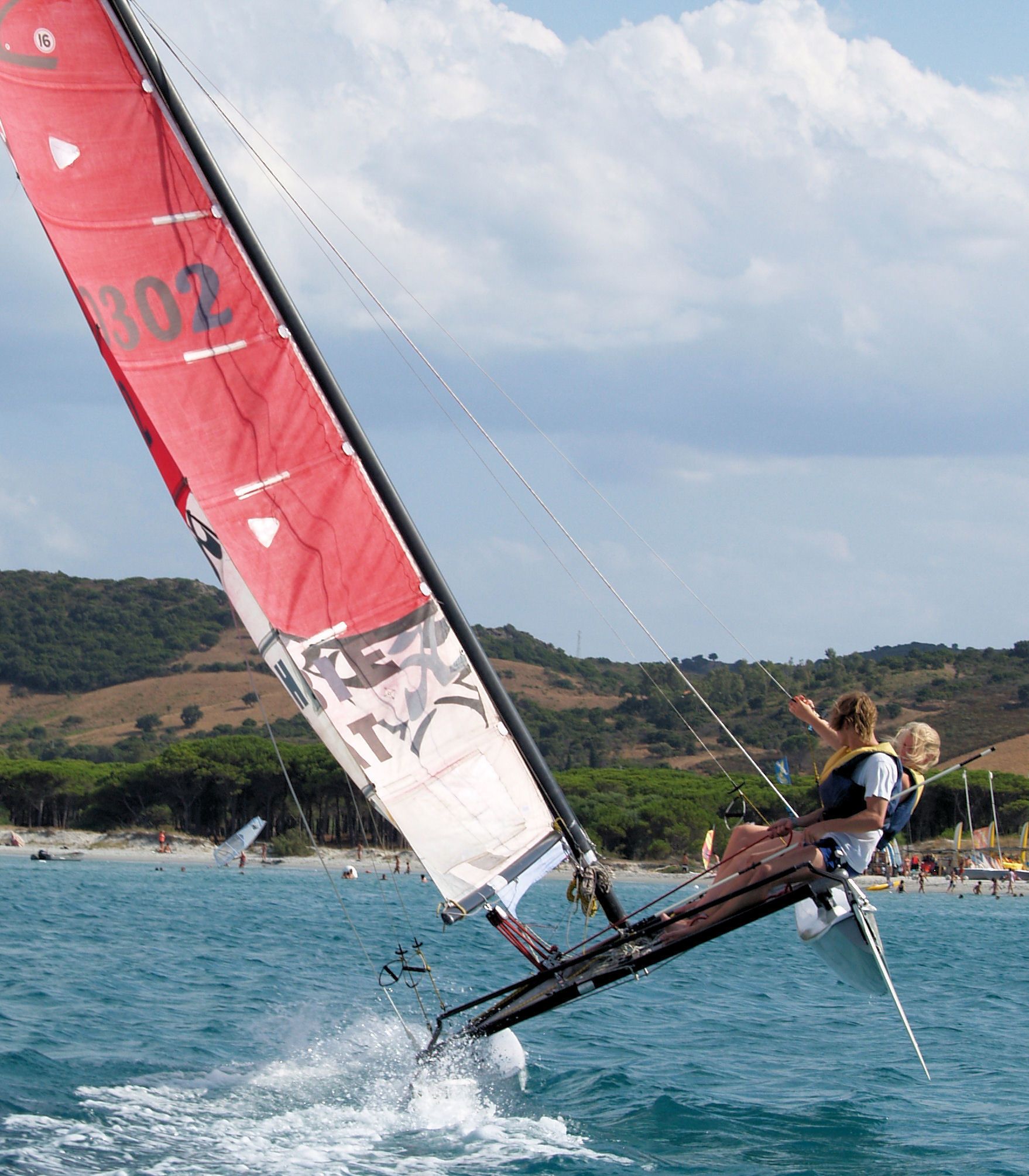 A sailboat with a red sail on a body of water.