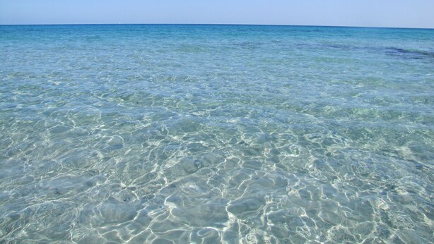 Una vista despejada de una playa con agua poco profunda y cristalina.