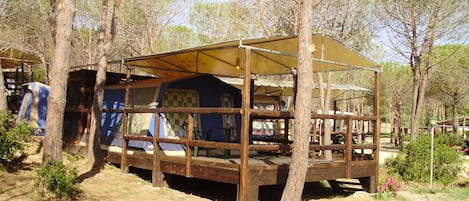 Une structure rustique en bois, dotée d’un espace de repos abrité et entourée d’arbres.