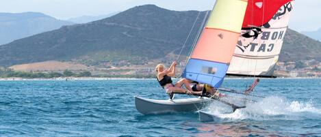 Uma pessoa praticando windsurf em um corpo de água, com uma vela colorida, cercada por uma paisagem montanhosa.