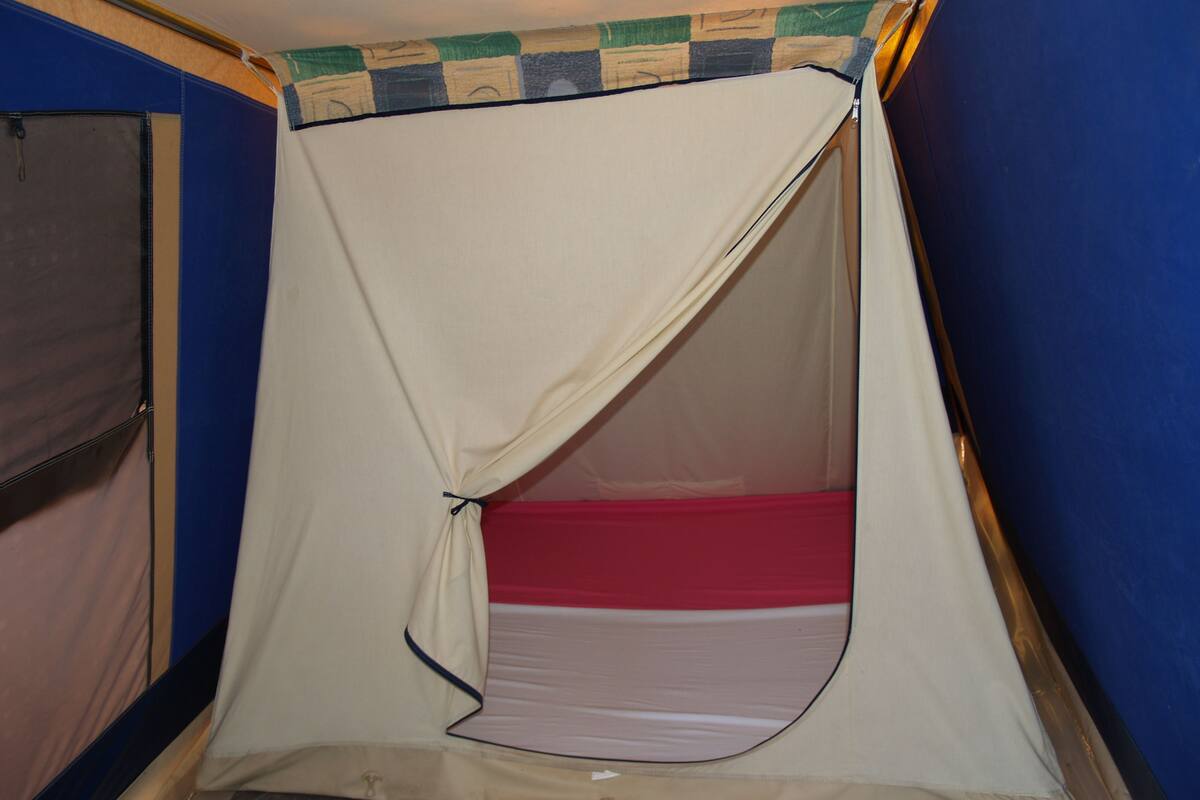 A tent-like structure with a red mattress inside, set against a blue wall with a checkered pattern at the top.