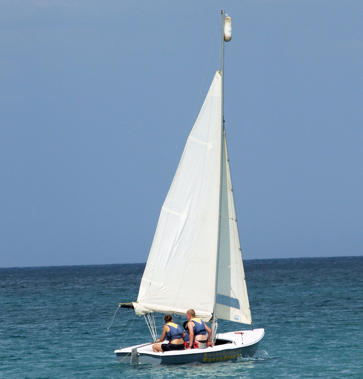 A sailboat with two people on board, sailing on a calm sea.