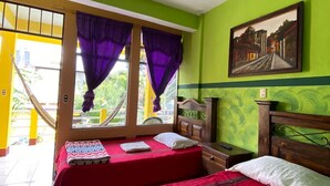 Una habitación con dos camas, una ventana con cortinas moradas, un cuadro en la pared y un ventilador de techo.