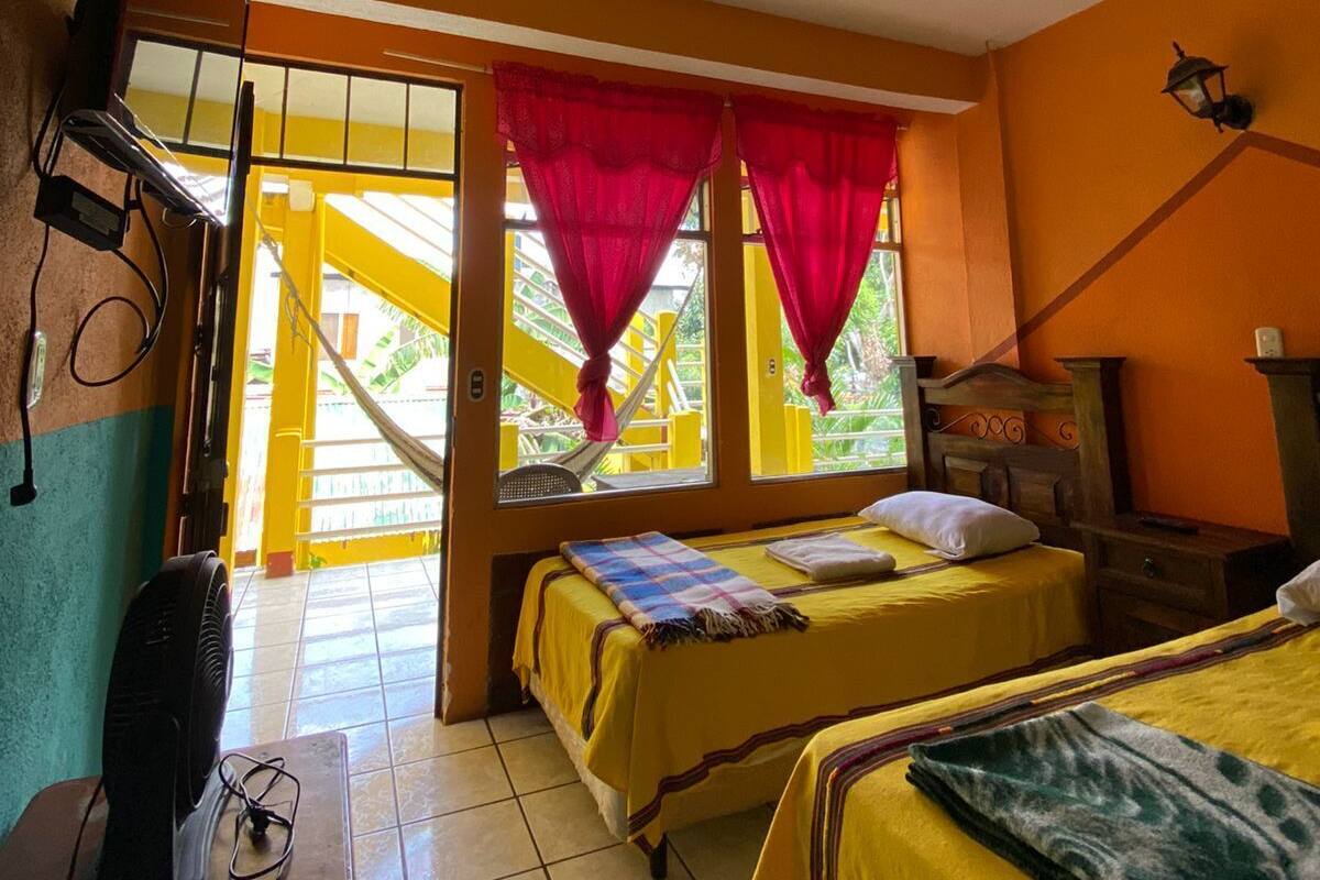 Une chambre avec deux lits, une télévision et une fenêtre avec des rideaux rouges.