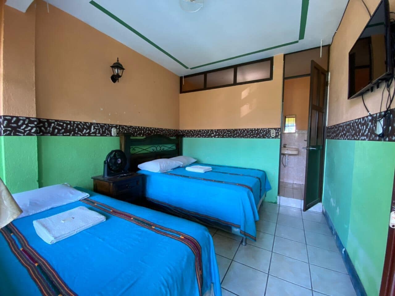 Una habitación con tres camas, un ventilador y una mesita pequeña.