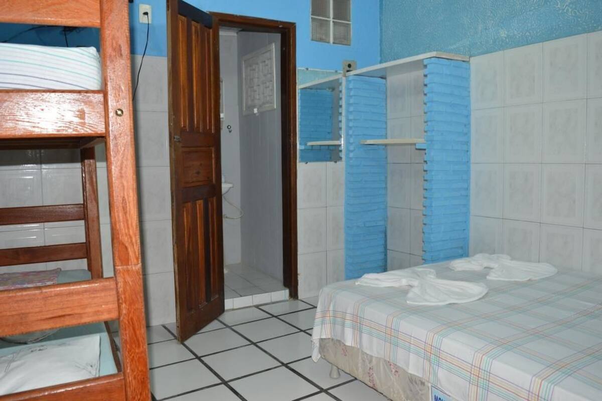 Ein Schlafzimmer mit Bett, einem Holzstuhl, einem Badezimmer mit Dusche und einer Tür zu einem weiteren Raum.
