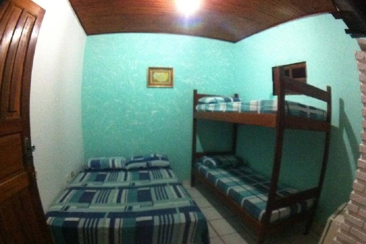 Ein Zimmer mit einem Etagenbett, einem Einzelbett mit gemusterten Betttextilien, einem kleinen gerahmten Bild an der Wand und einer Holztür.