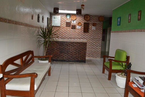 A reception area with a brick wall, wooden benches, a green chair, and a potted plant.