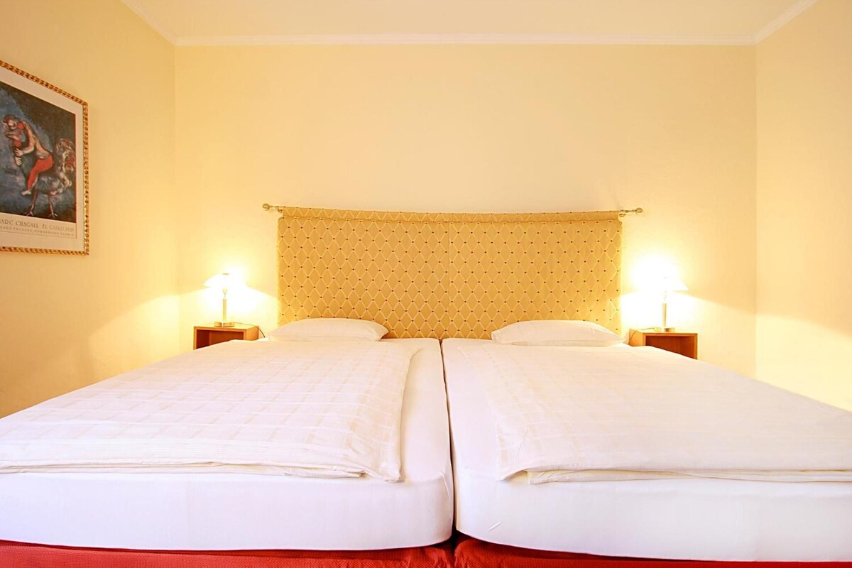 Uma cama de casal com cabeceira, duas mesas de cabeceira e um quadro na parede.