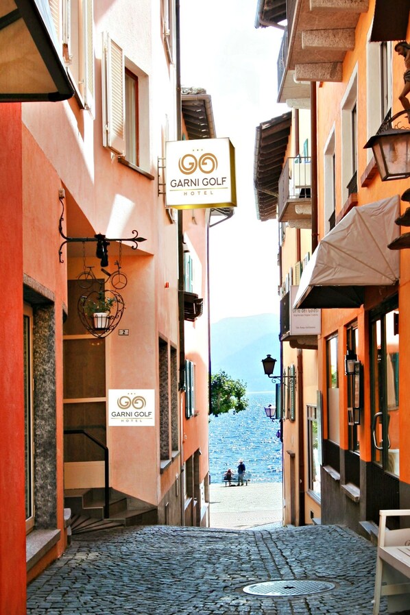 Rua de paralelepípedos estreita que conduz a uma vista do mar, com uma placa para o Garni Golf Hotel.