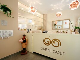 Zona de recepción con mostrador, una figura decorativa, un espejo y un cartel que dice "GARNI GOLF".