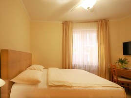 Una habitación de hotel con cama, cortinas, escritorio y televisión.