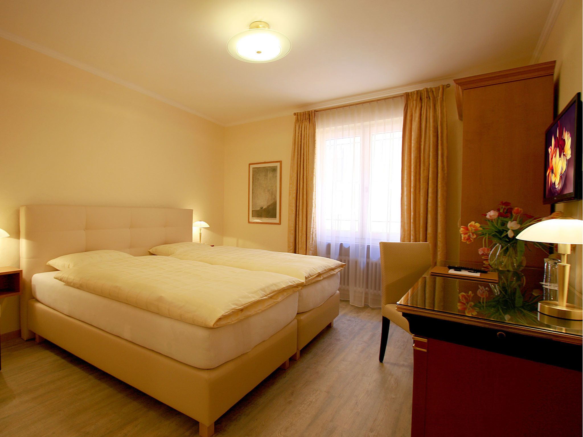 Una habitación de hotel con una cama doble, un escritorio con lámpara, una silla y un jarrón con flores.