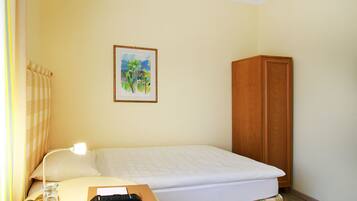 A small, neatly arranged bedroom with a single bed, a nightstand, a lamp, a remote control, and a framed picture on the wall.