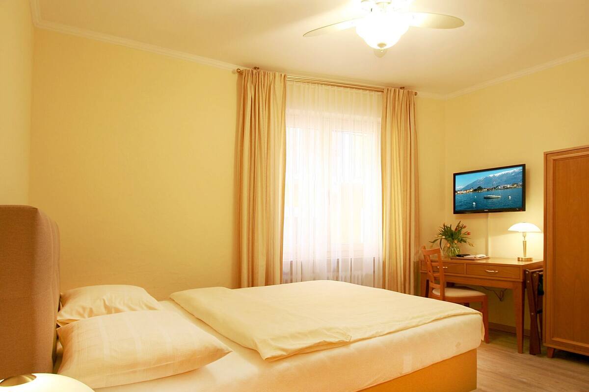 Una habitación de hotel con cama, escritorio, silla, televisor y ventilador de techo.