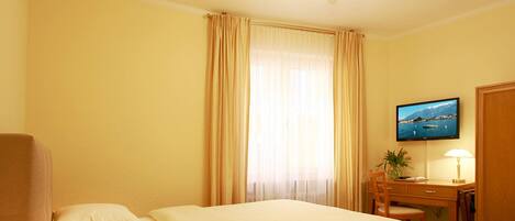 A hotel room with a bed, a desk, a chair, a television, and a ceiling fan.