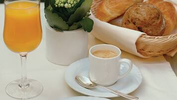 A breakfast setting with a glass of orange juice, a cup of coffee, a small plant, and a basket of croissants.