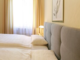 Habitación de hotel con dos camas, una mesita de noche con lámpara y un cuadro en la pared.