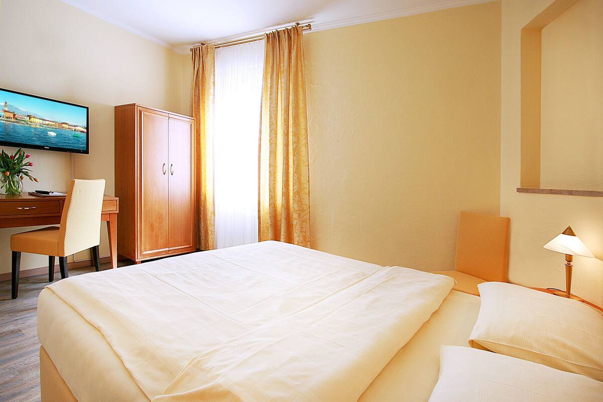 Habitación de hotel con cama, escritorio, silla, televisión y lámpara.