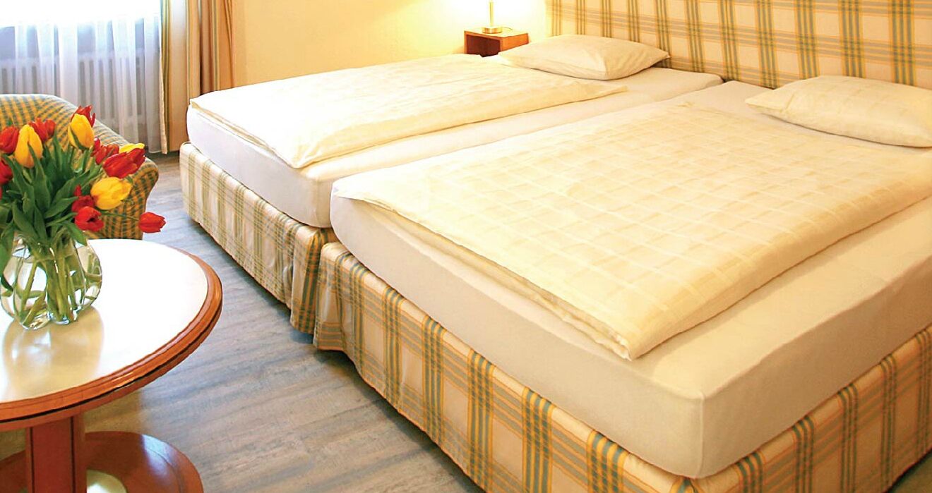 A hotel room with two beds, a round table with a vase of tulips, and a nightstand with a lamp.
