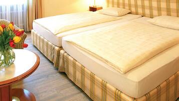 Una camera d'albergo con due letti, un tavolino rotondo con un vaso di tulipani e un comodino con una lampada.
