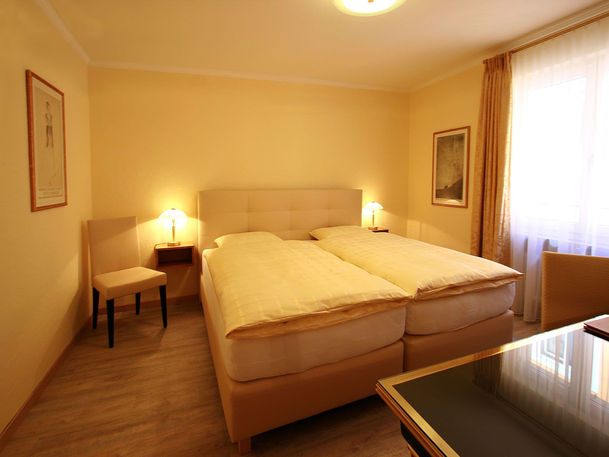 Ein Hotelzimmer mit einem Doppelbett, zwei Nachttischen mit Lampen, einem kleinen Sessel und einem Schreibtisch.