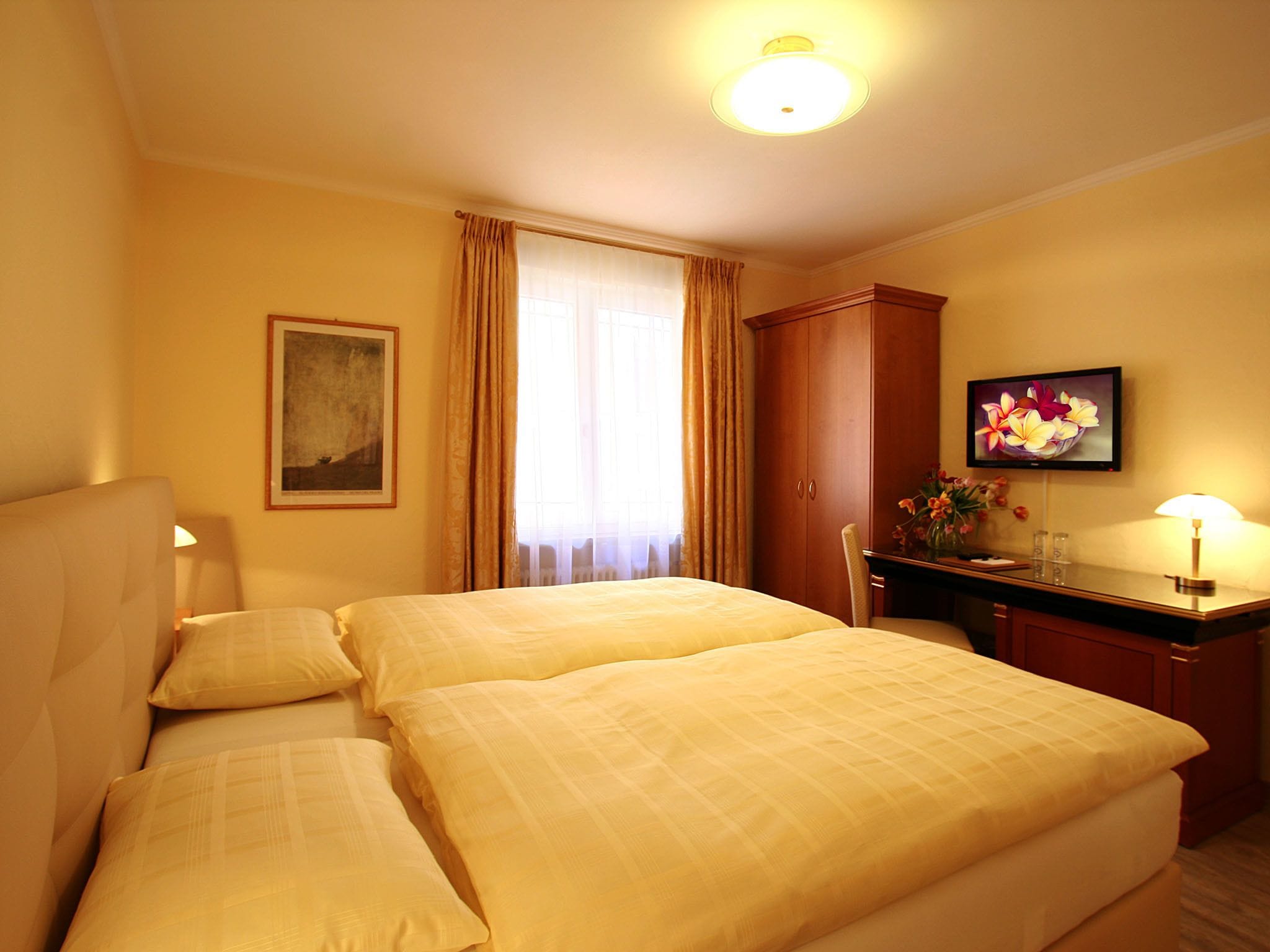 Ein Hotelzimmer mit zwei Betten, einem Schreibtisch, einem Sessel, einem Fernseher und einem Gemälde an der Wand.