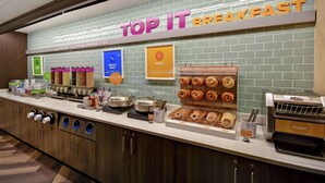 Una estación de desayuno con un letrero que dice "TOP IT BREAKFAST" y diversas opciones de comida como waffles, huevos y pasteles.