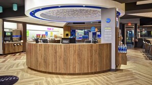 Zona de recepción de un hotel con un mostrador de madera, un quiosco digital y un cartel que dice 'Top IT'.