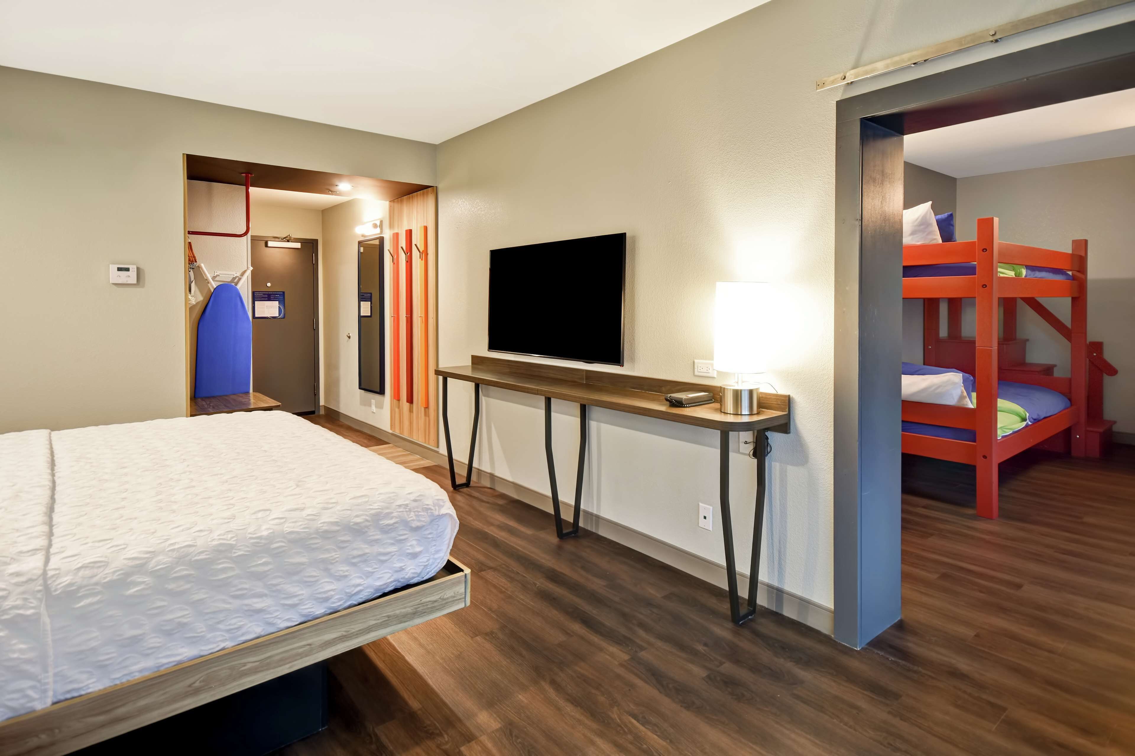 A hotel room with a bed, a TV, a desk, and a bunk bed.