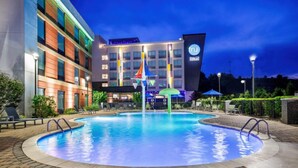 Un hotel con piscina, mobiliario exterior y una fachada bien iluminada.