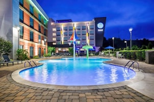 Un hotel con piscina, mobiliario exterior y una fachada bien iluminada.