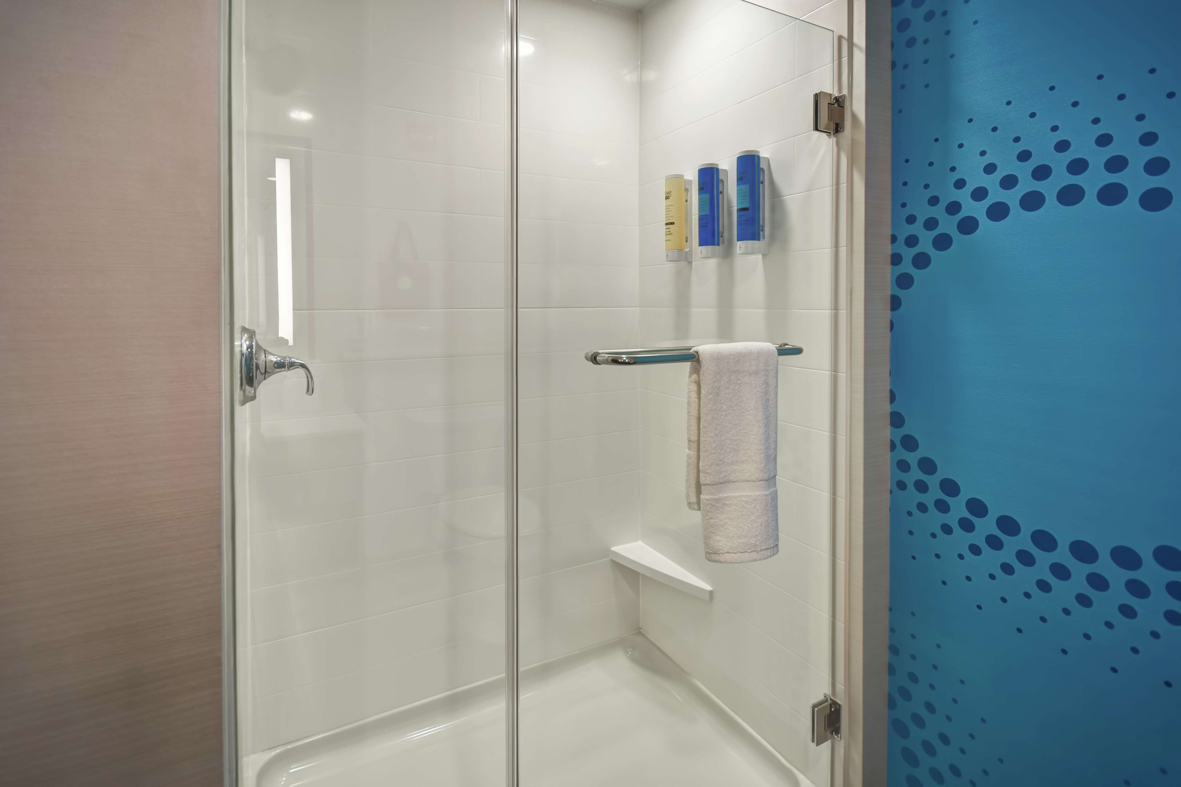 A glass-enclosed shower with a white tiled wall, a towel rack with a towel, and a blue wall with a dotted pattern.