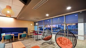 A modern lounge area with seating, tables, and large windows offering a view of the cityscape. - Tru by Hilton Fort Wayne, IN (Fort Wayne)