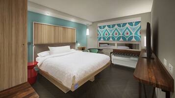 A modern hotel room with a large bed, a desk, a television, and a unique wall art piece.
