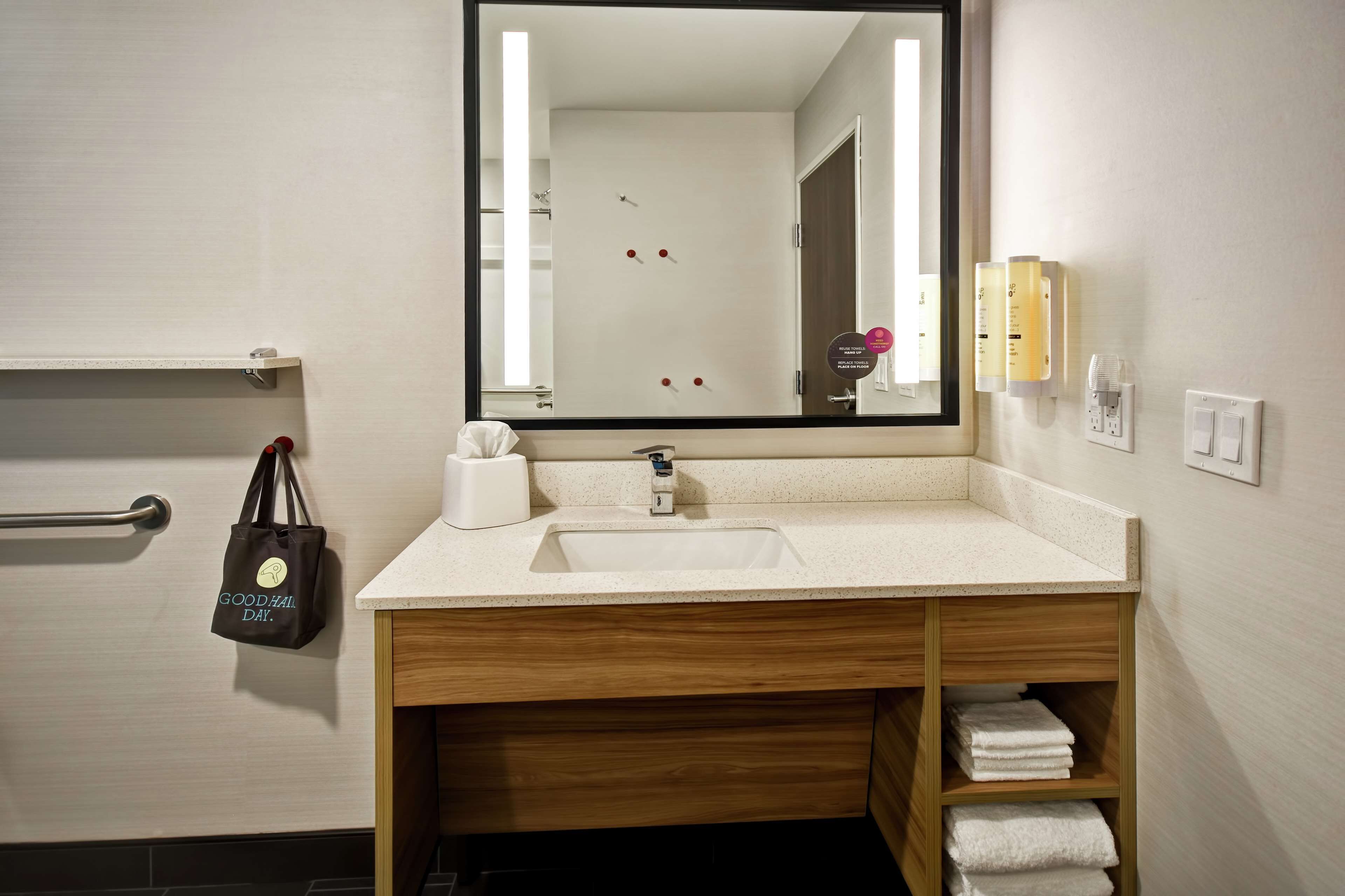 A modern bathroom with a wooden vanity, a large mirror, a sink, and a towel rack.