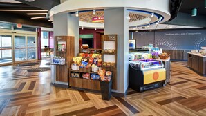 A modern breakfast area with a self-serve station, a display of snacks, and a view of the dining area. - Tru by Hilton Fort Wayne, IN (Fort Wayne)