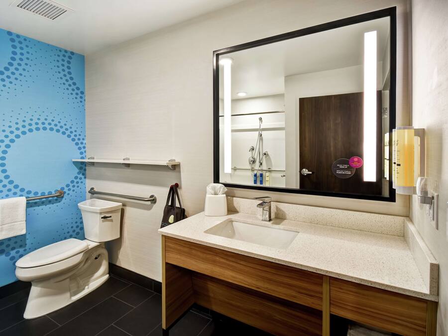 Un baño con inodoro blanco, lavamanos con espejo y pared azul con diseño de lunares.