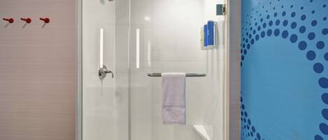 A modern bathroom with a glass shower enclosure, a white sink, and a blue wall with a dot pattern.
