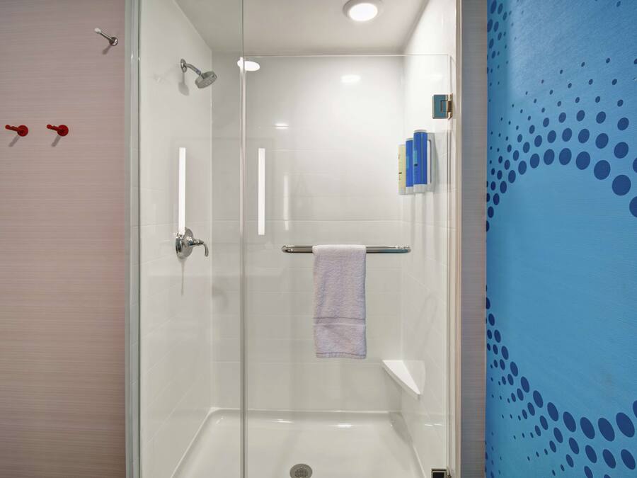 Casa de banho moderna com cabine de duche em vidro, lavatório branco e parede azul com padrão de pontos.