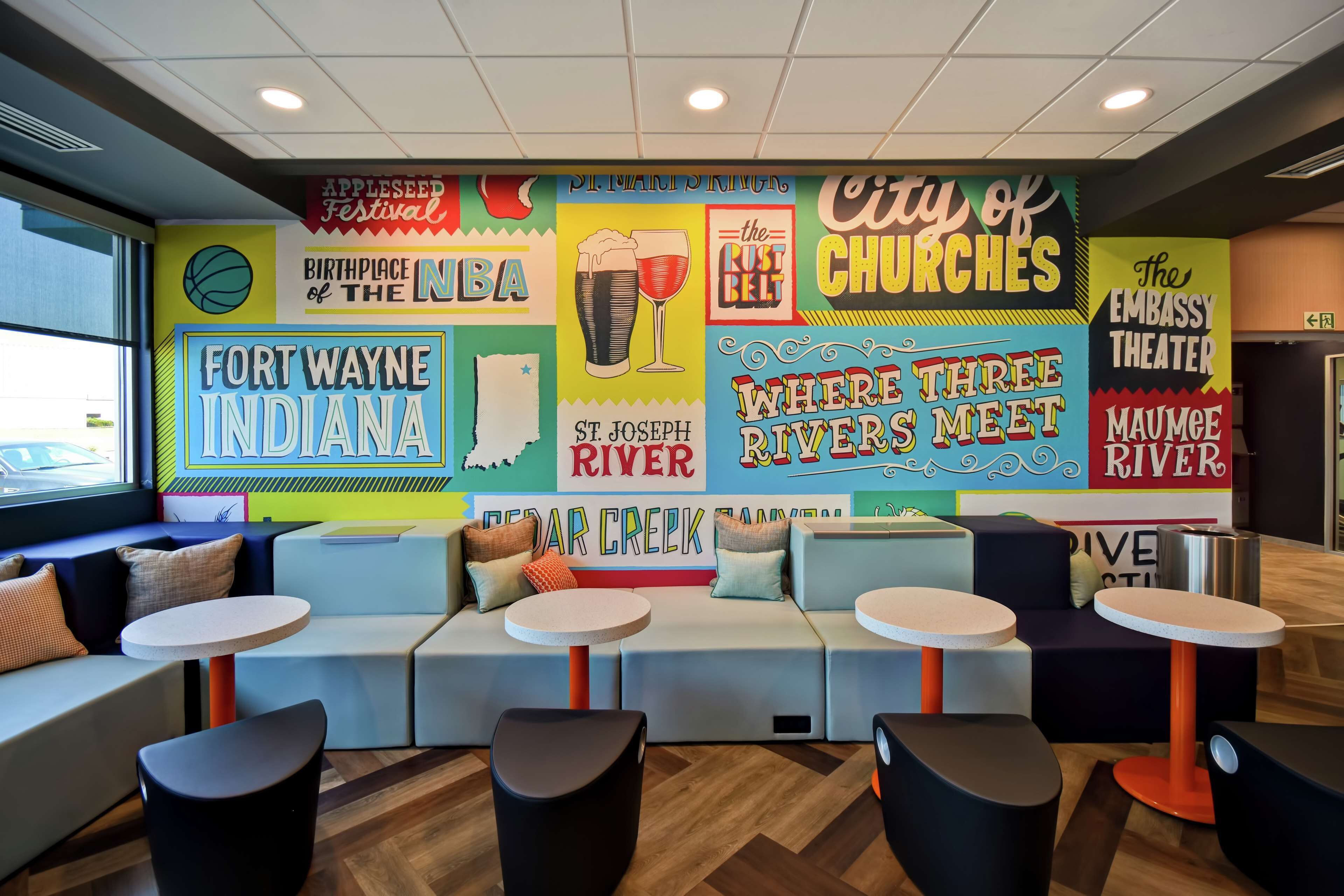Un interior vibrante con zonas de estar y un mural que muestra puntos emblemáticos y eventos locales.